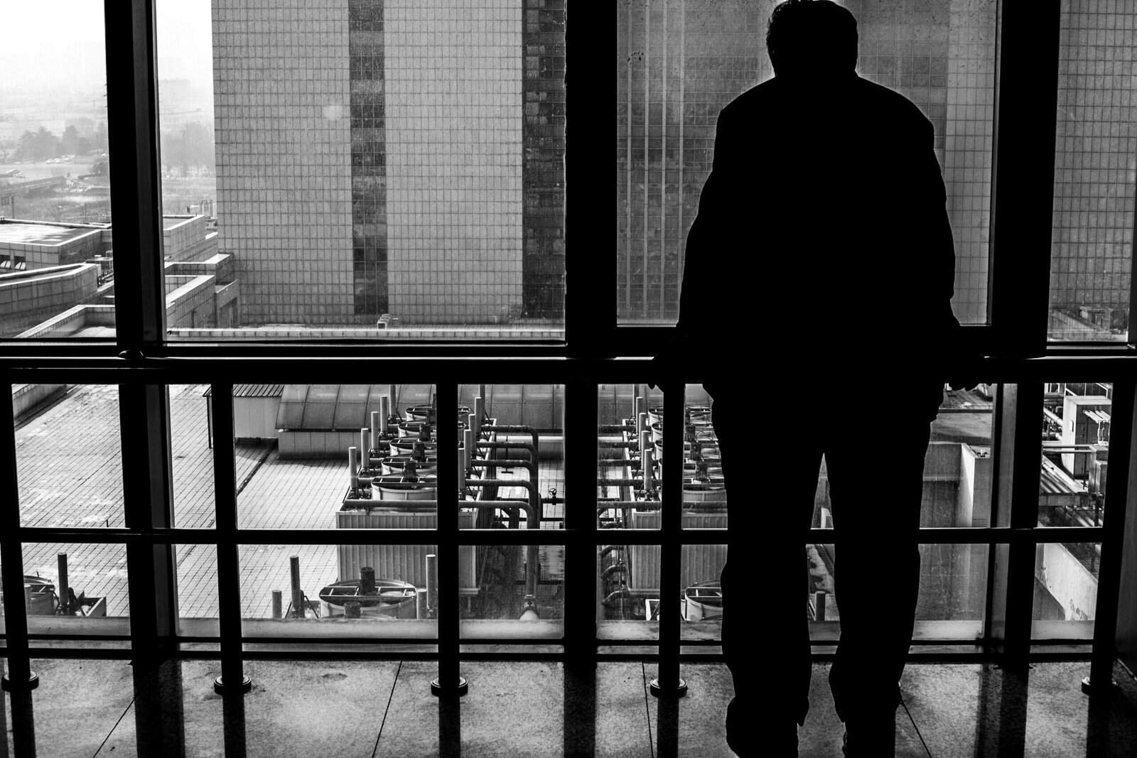 man standing staring out of a window, over a industrial landscape
